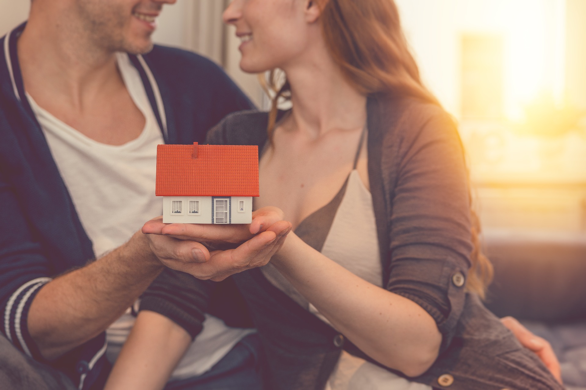 Two people holding a model property in their hands, smiling at each other; our Conveyancing Solicitors in Lytham discuss different types of property ownership and how our team can assist with this.