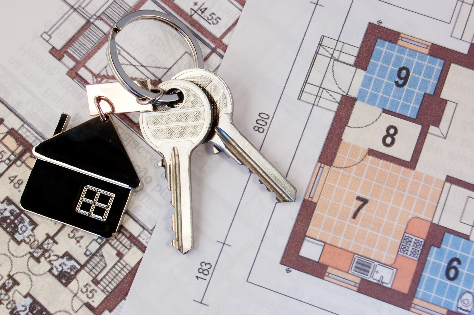 A pair of silver keys, with a black house keyring, laid on plans for a property