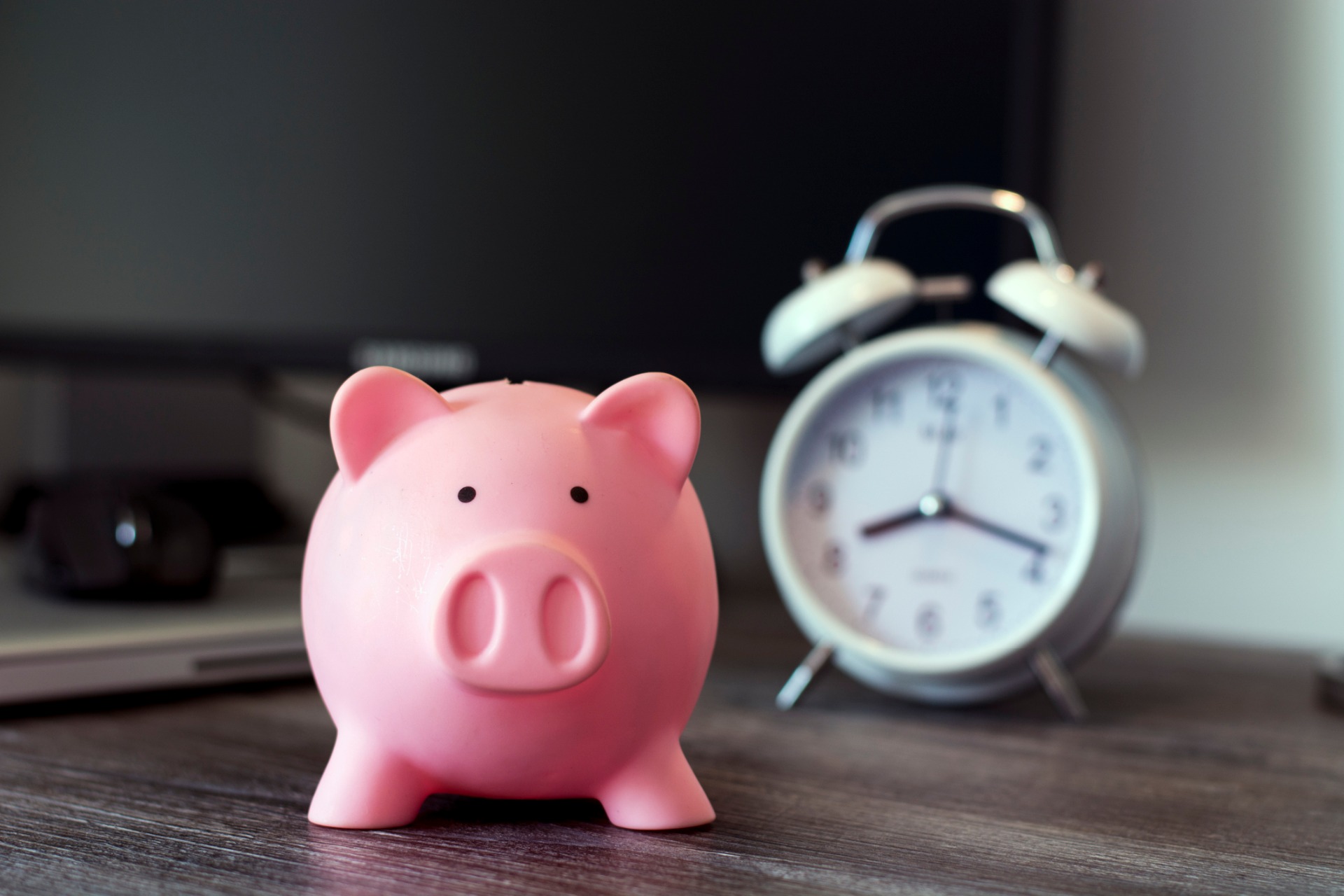 A piggy bank in front of a clock: Our Solicitors in Lancaster discuss hourly-rate charges and fixed fees