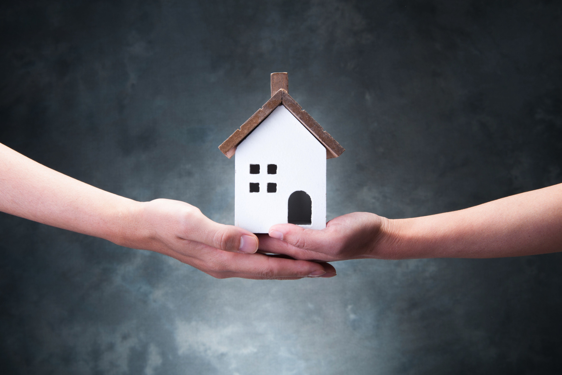 Two people, joining hands, holding a property model.