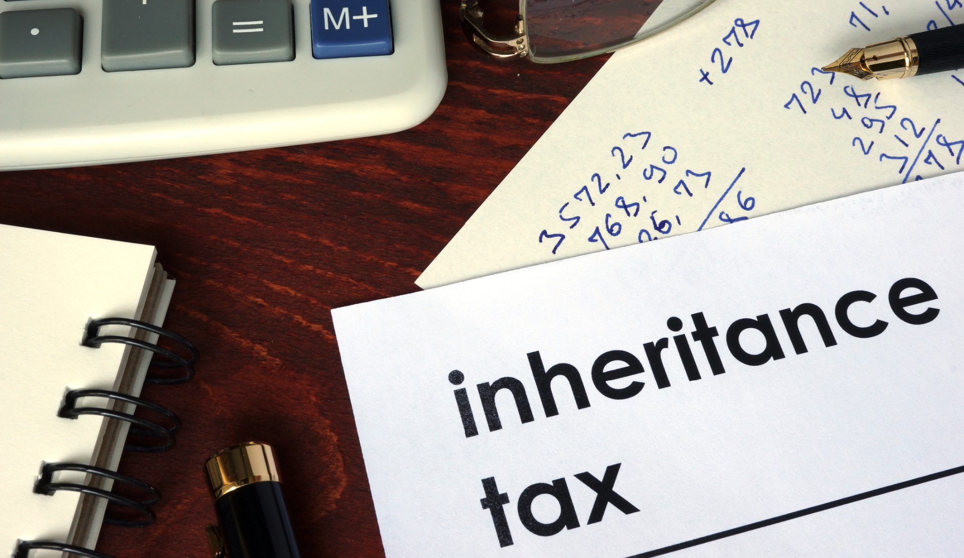 A form saying 'Inheritance Tax' and a pile of papers underneath with workings out, and the edge of a notebook, a calculator and some glasses.