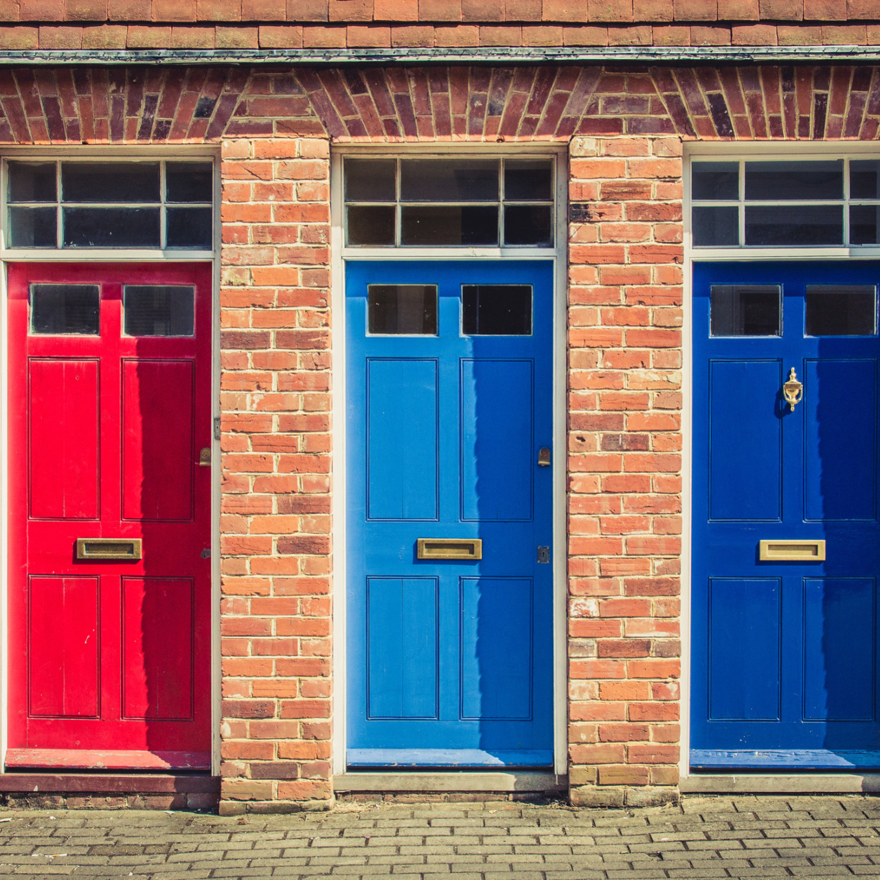 Three symmetrical doors painted in different colours: red, light blue and darker blue.