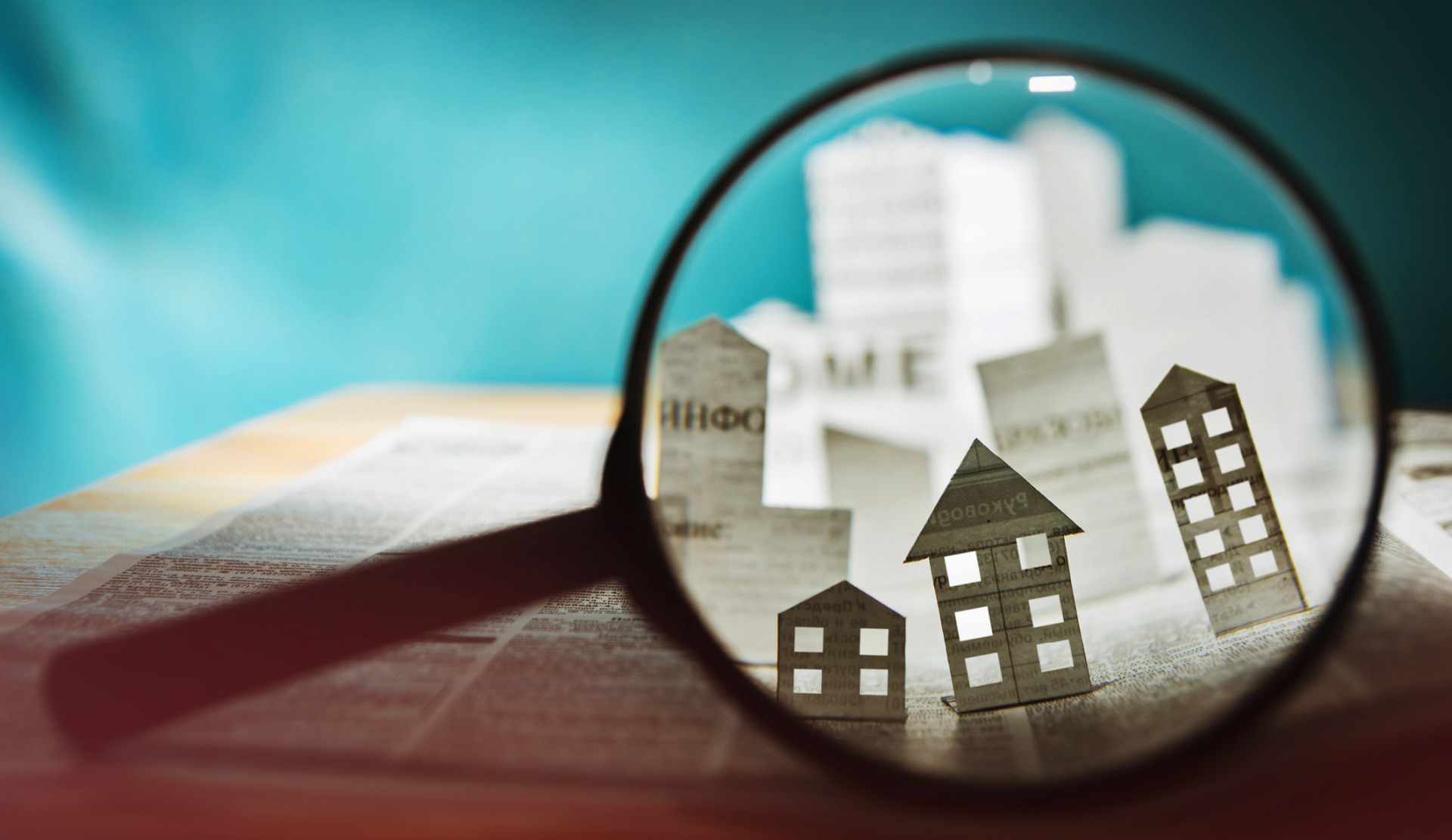 A black magnifying glass held up against some little paper cut-out houses