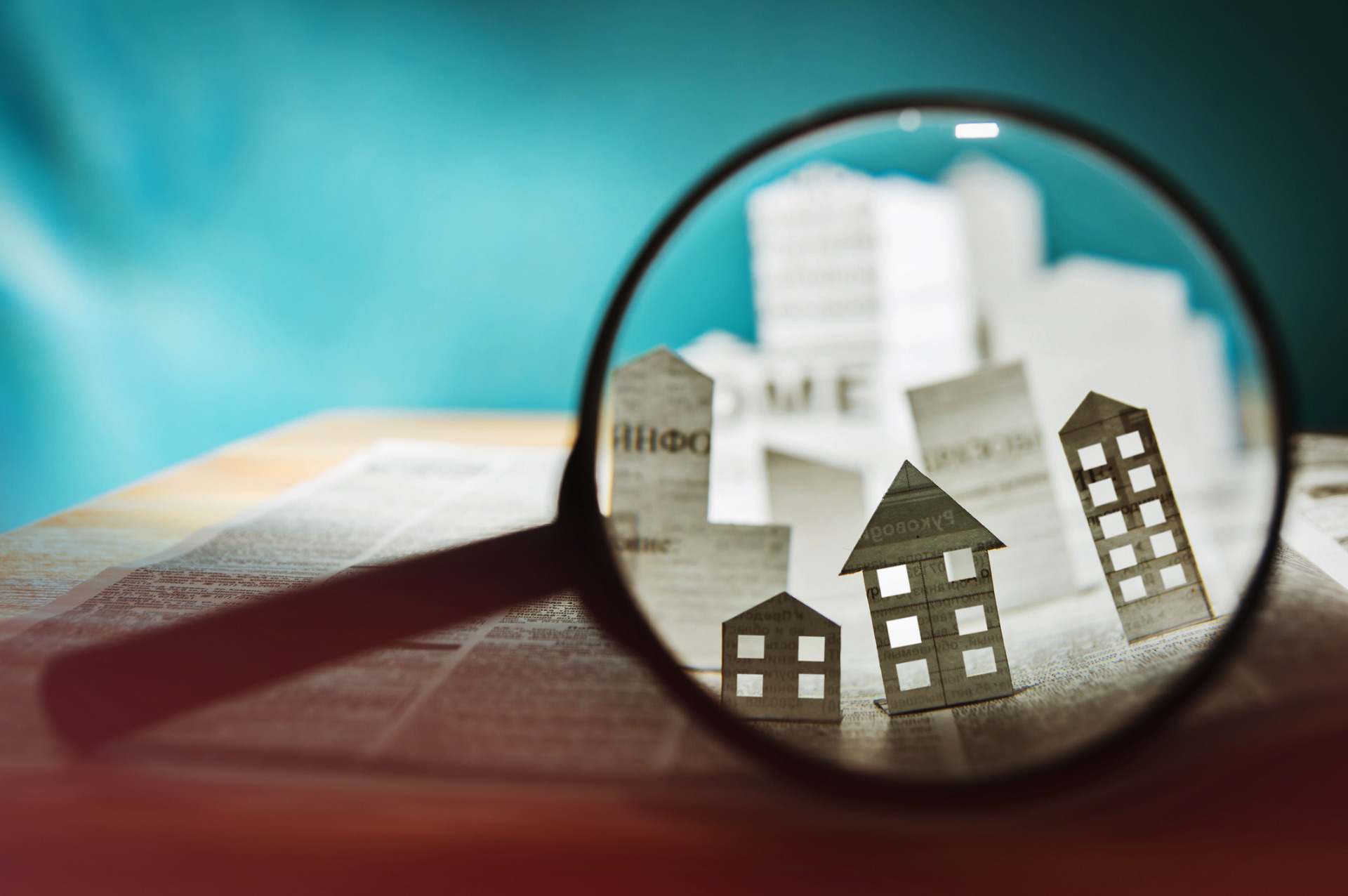 A magnifying glass looking at a book, with cut out miniature houses.
