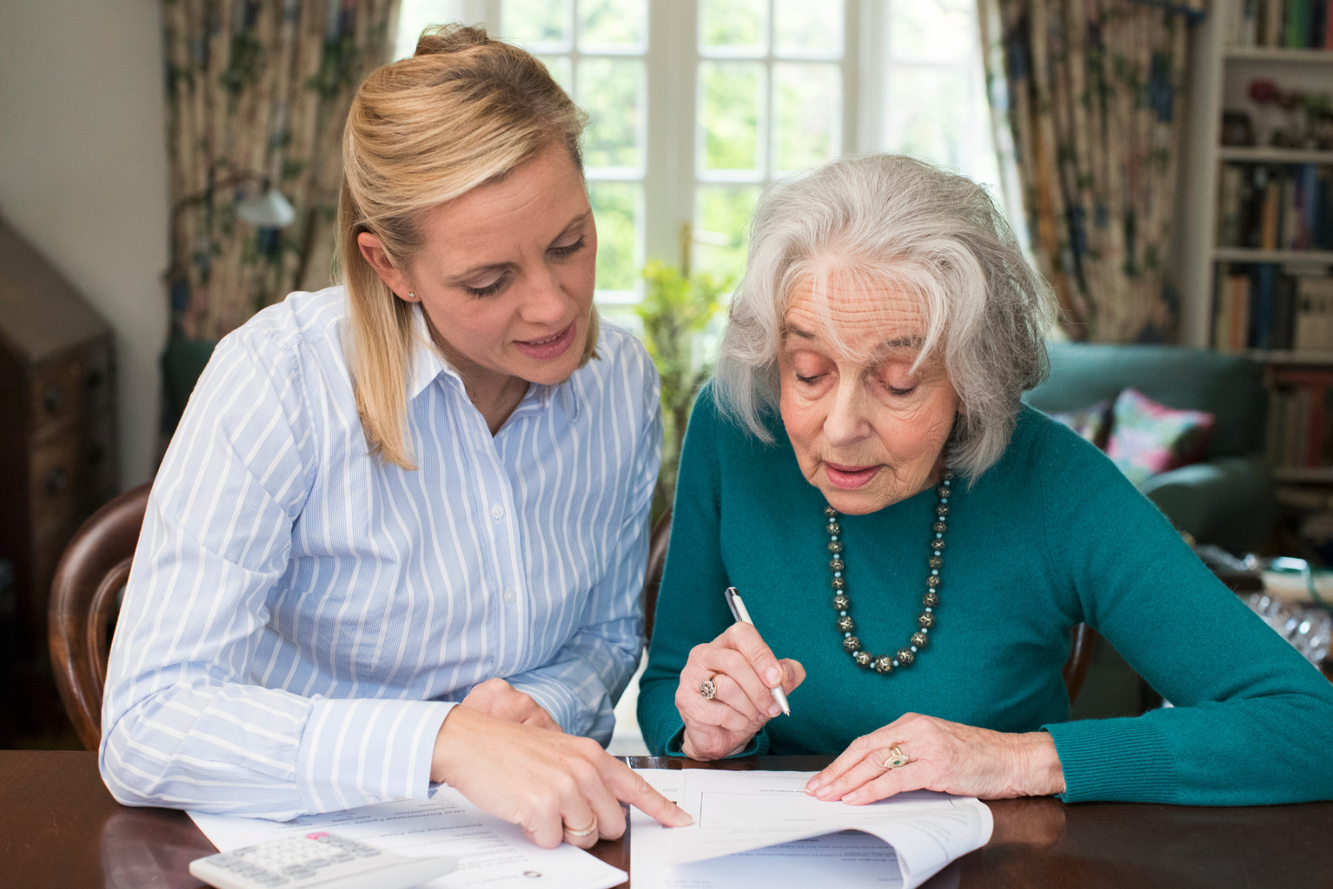 A lady helping an older lady to read through some documents.