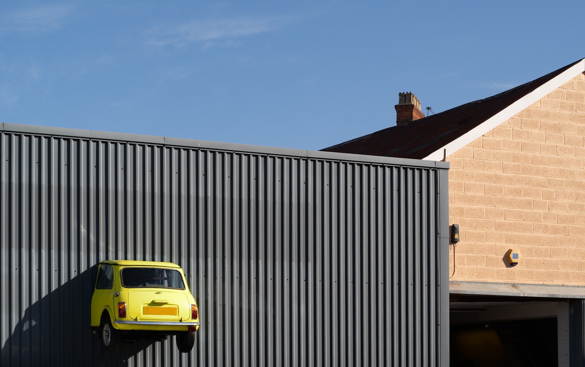 A yellow mini that has driven into a wall, and is half-sticking out.