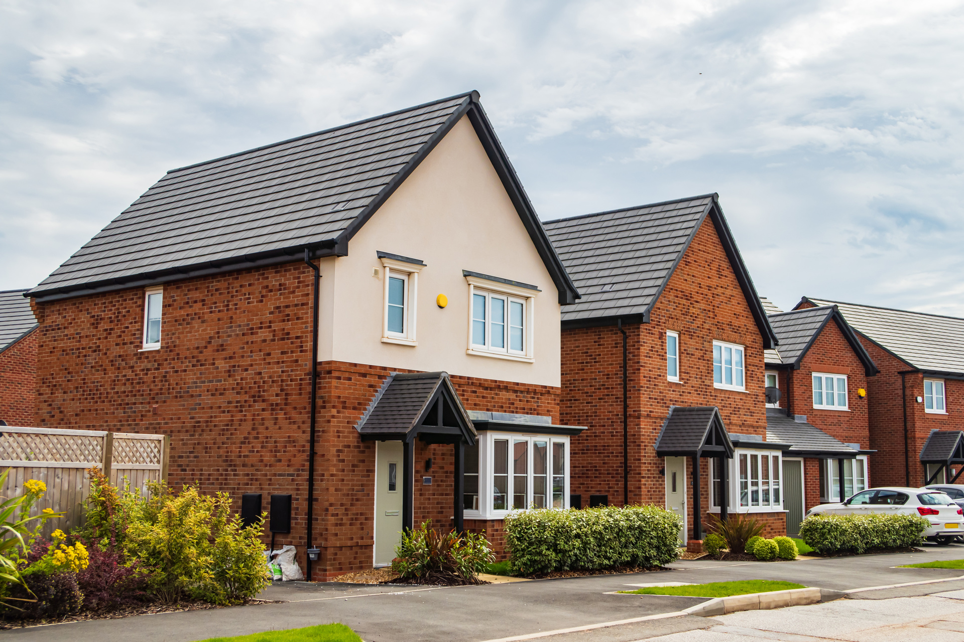 A new build housing estate, showing three detached houses, with similar exteriors, driveways and shrubbery; our Conveyancing Solicitors in Preston discuss new build housing trends in 2024.