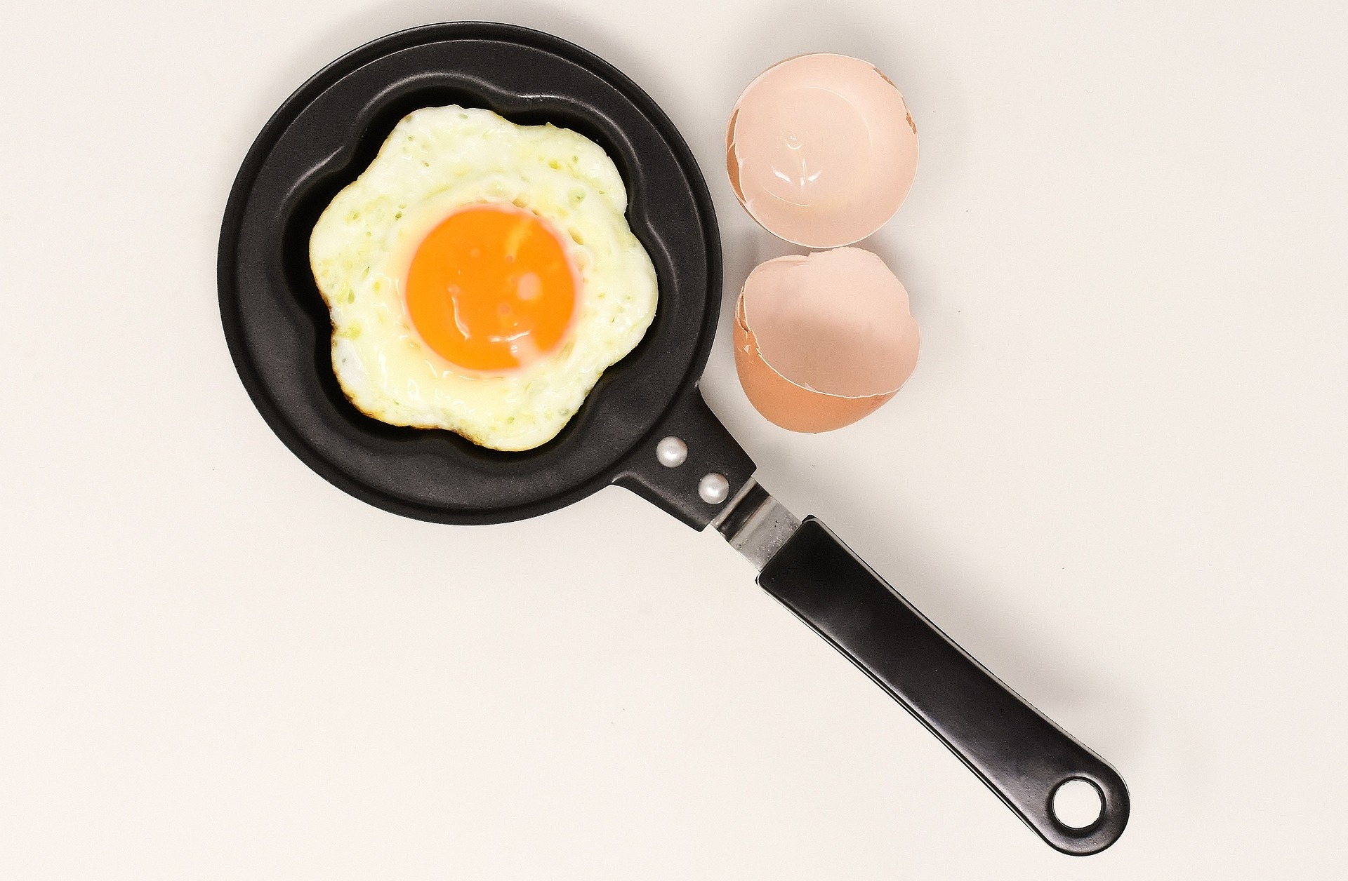 An egg pan, with a flower-shaped, cooked egg, and an egg shell nearby; our no win no fee solicitors specialise in egg allergy reaction compensation claims.