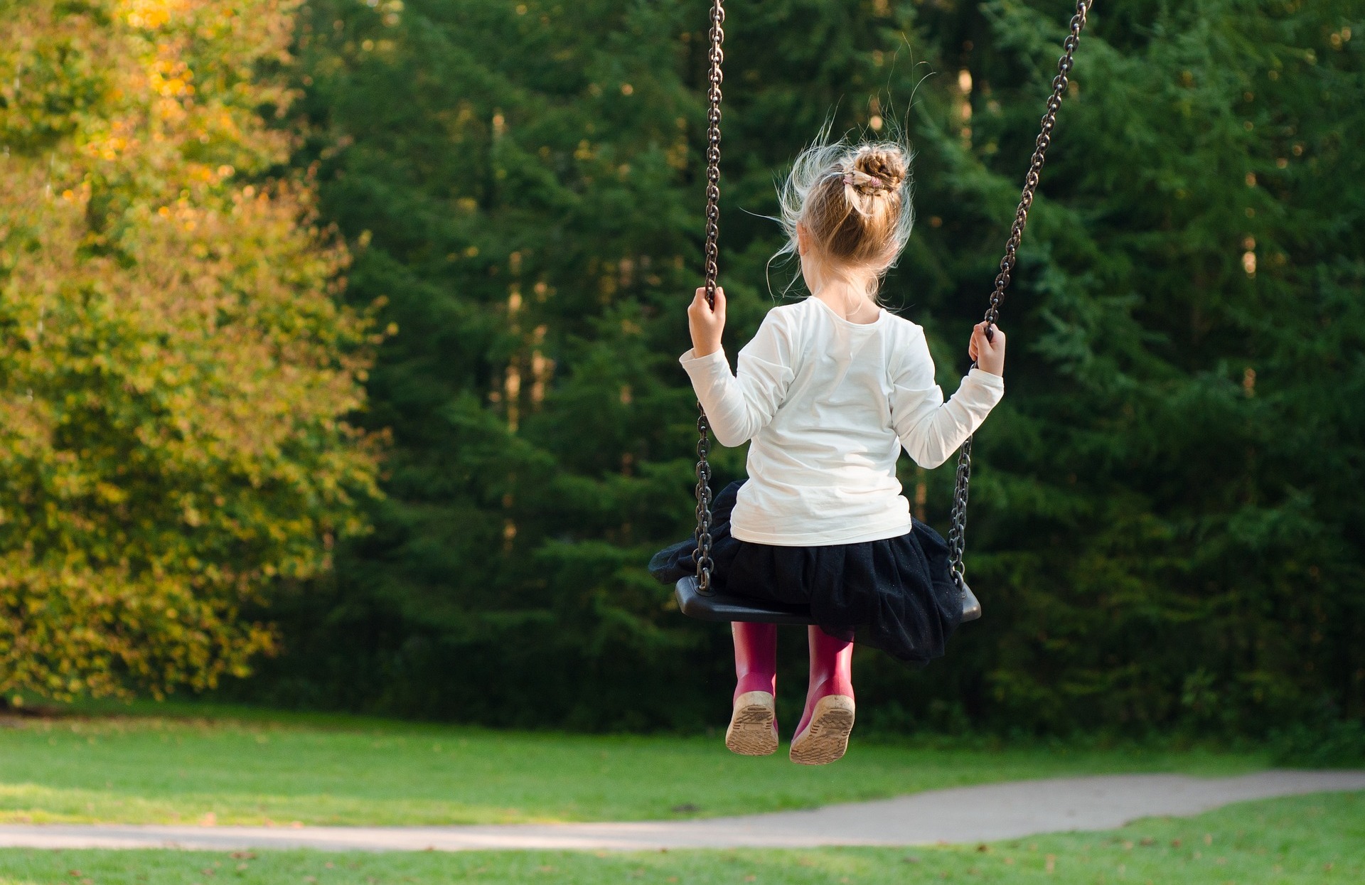 A young person swinging on a swing in a park, with open fields and lots of trees.  Click the picture, or the link below, to go to our personal injury solicitors’ no win no fee child injury claims page.