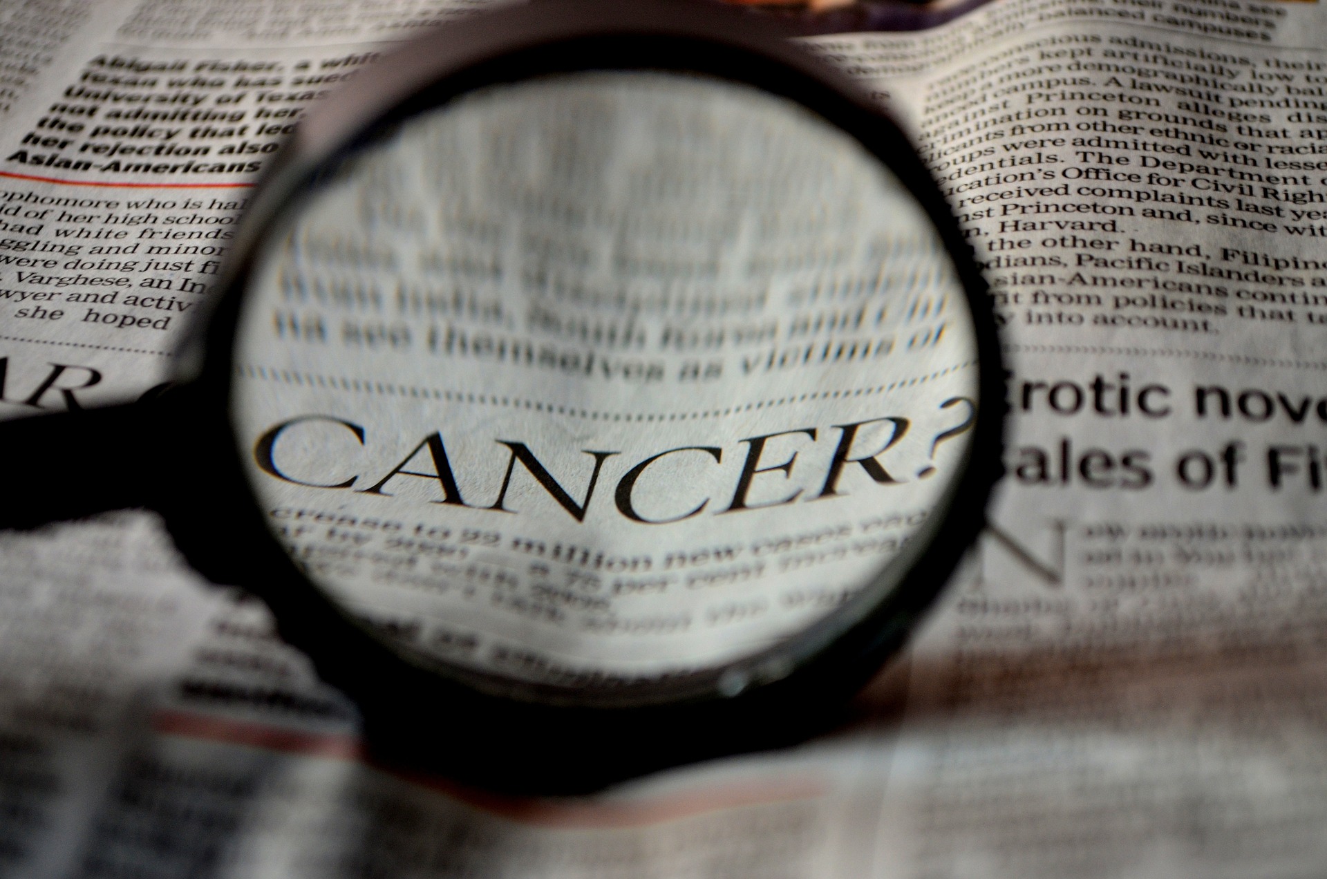 A newspaper with the word “Cancer” magnified - our medical negligence compensation solicitors can help you make a no win no fee claim.  Click on this link to visit our Cancer negligence compensation page.