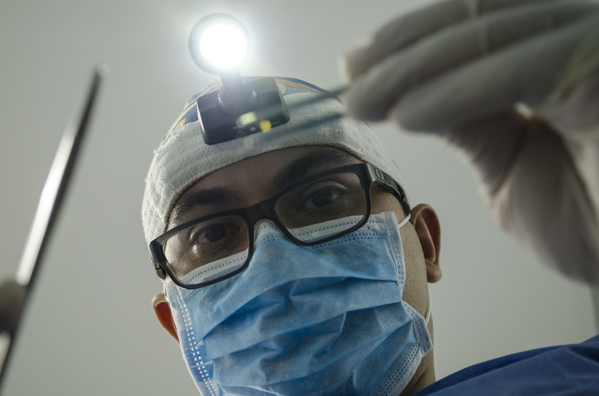 A dentist wearing protective gear, holding dental equipment over a person- our medical negligence compensation solicitors can help you make a no win no fee claim.  Click on this link to visit our dental negligence compensation claim page.