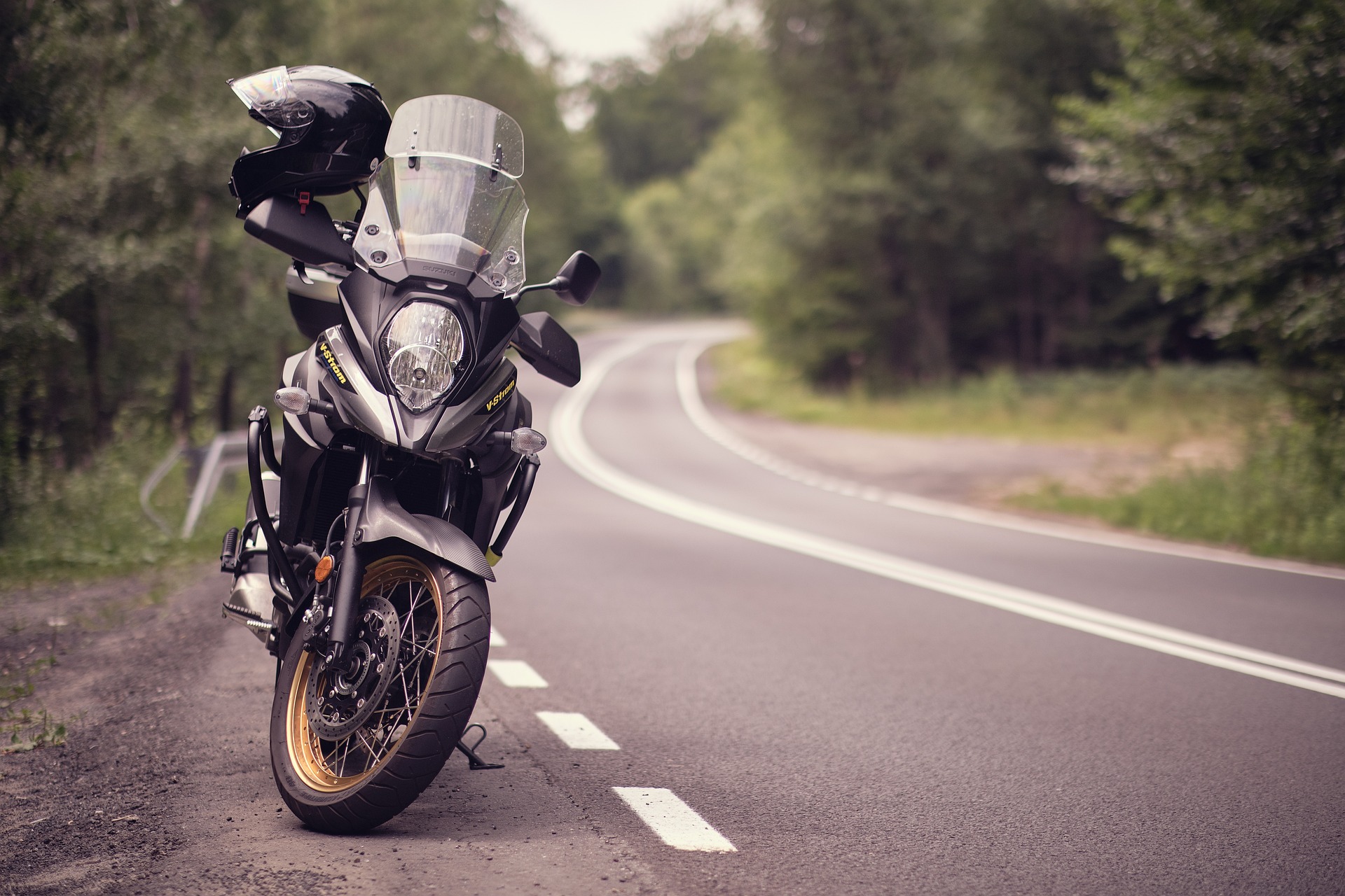 A Motorcycle parked on the side of a road, running through a forest; our No Win No Fee Solicitors discuss making an injury compensation claim if you are a motorcycle user who has been injured through no fault of your own on the road.