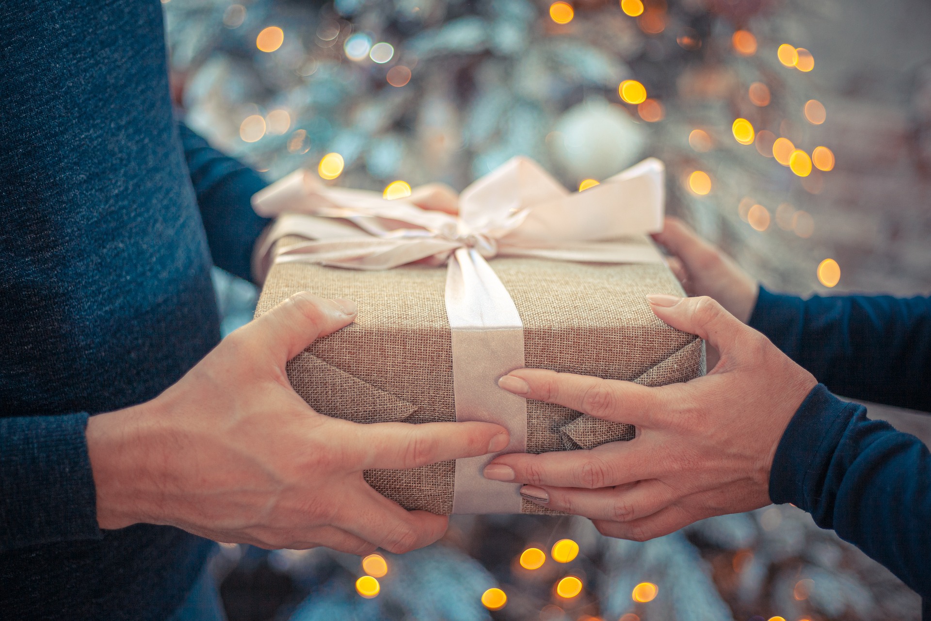 Two people passing a wrapped gift between them; our Conveyancing Solicitors in Lytham discuss the pros and cons of gifting property to your children during your lifetime.