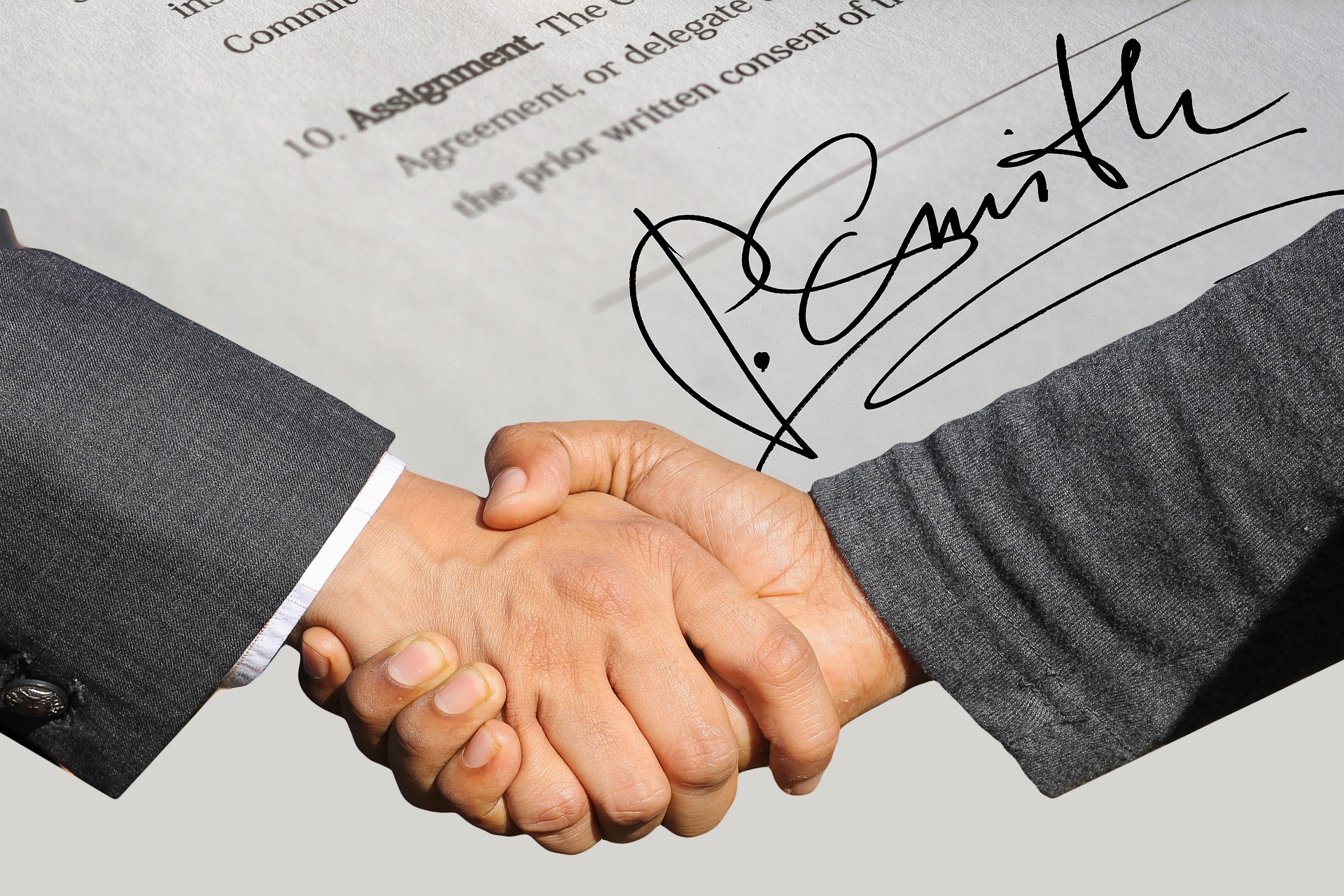 Part of a contract, with a signature at the bottom, and two people shaking hands to agree the terms; our Conveyancing Solicitors in Preston discuss exchange of contracts and completion in Conveyancing.
