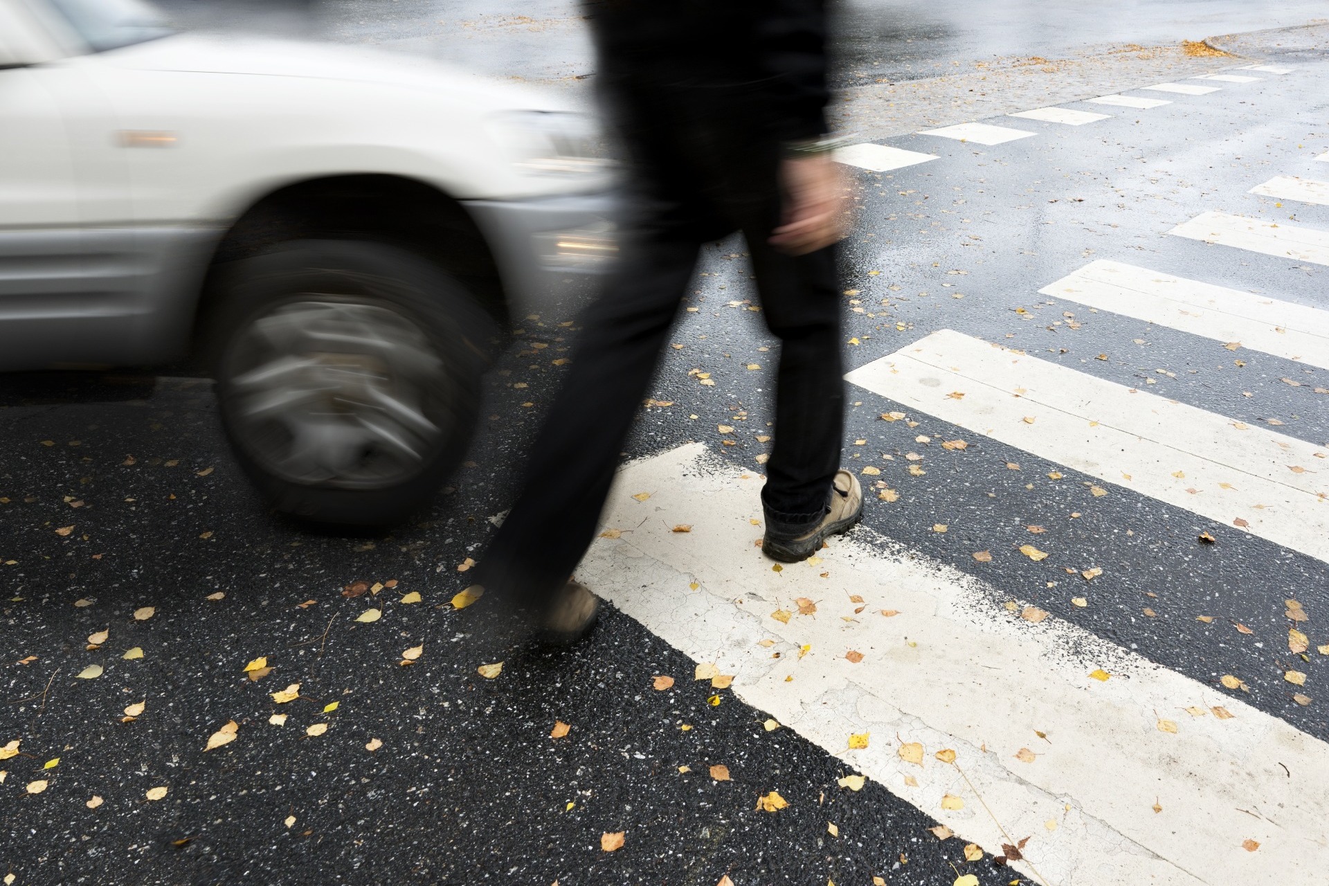 A person crossing a zebra crossing, about to be hit by a car.