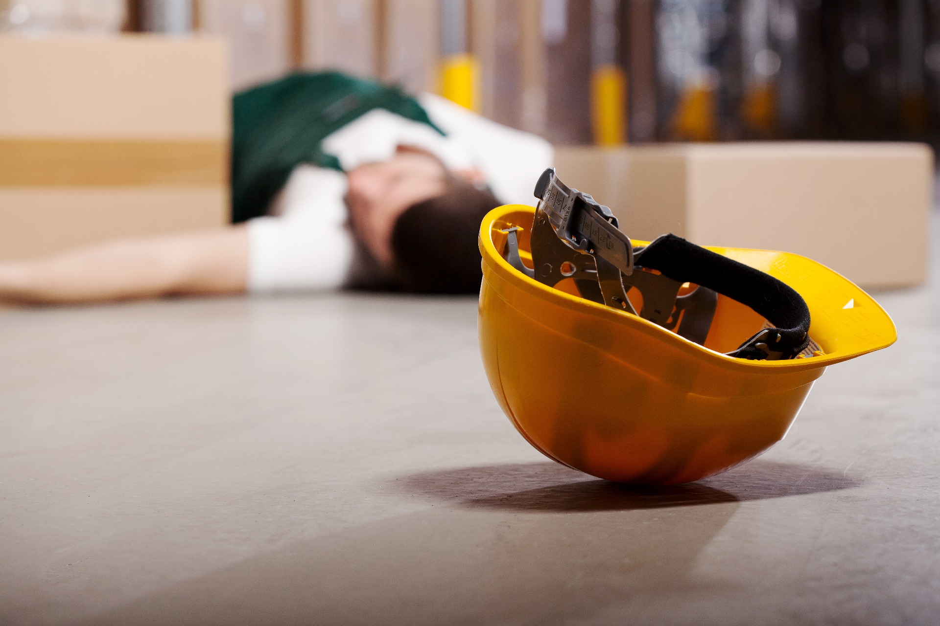 A man who has fallen over at work, with a hard hat resting next to his head.
