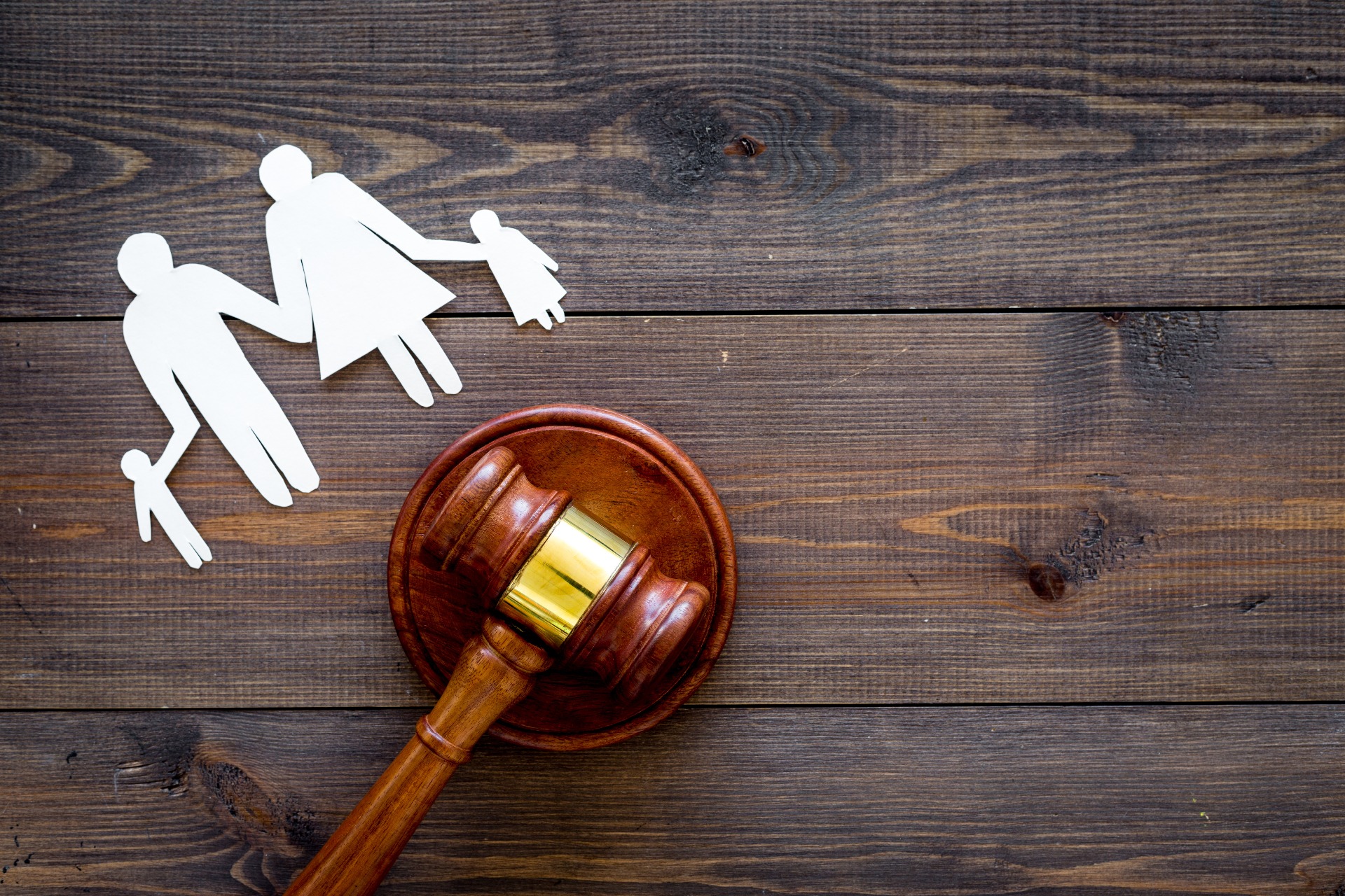 A wooden Gavel used by Judges on a wooden surface, below a paper cut out of two parents and two children.