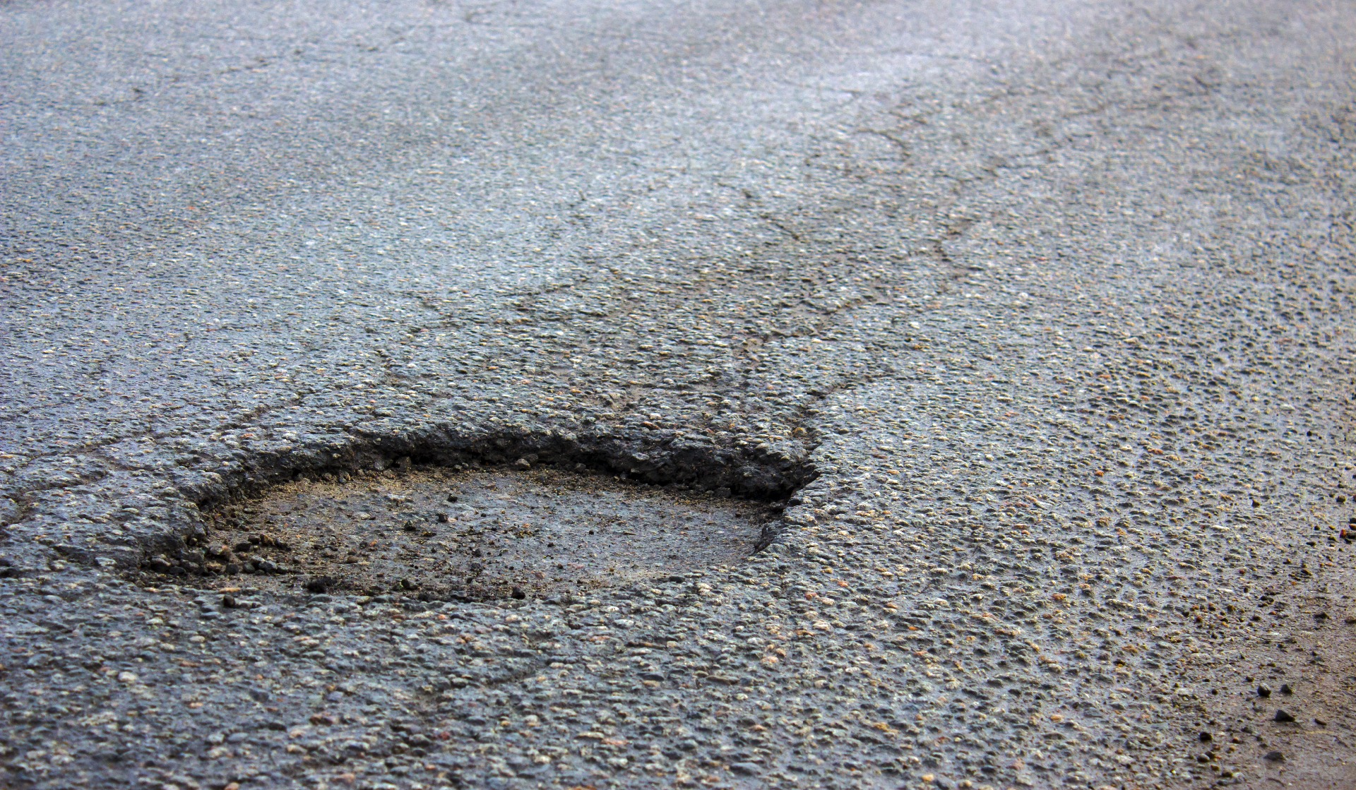 A large pothole in the middle of a road; our No Win No Fee Personal Injury solicitors can help you make an injury compensation claim for the injuries you suffer due to damaged roads.