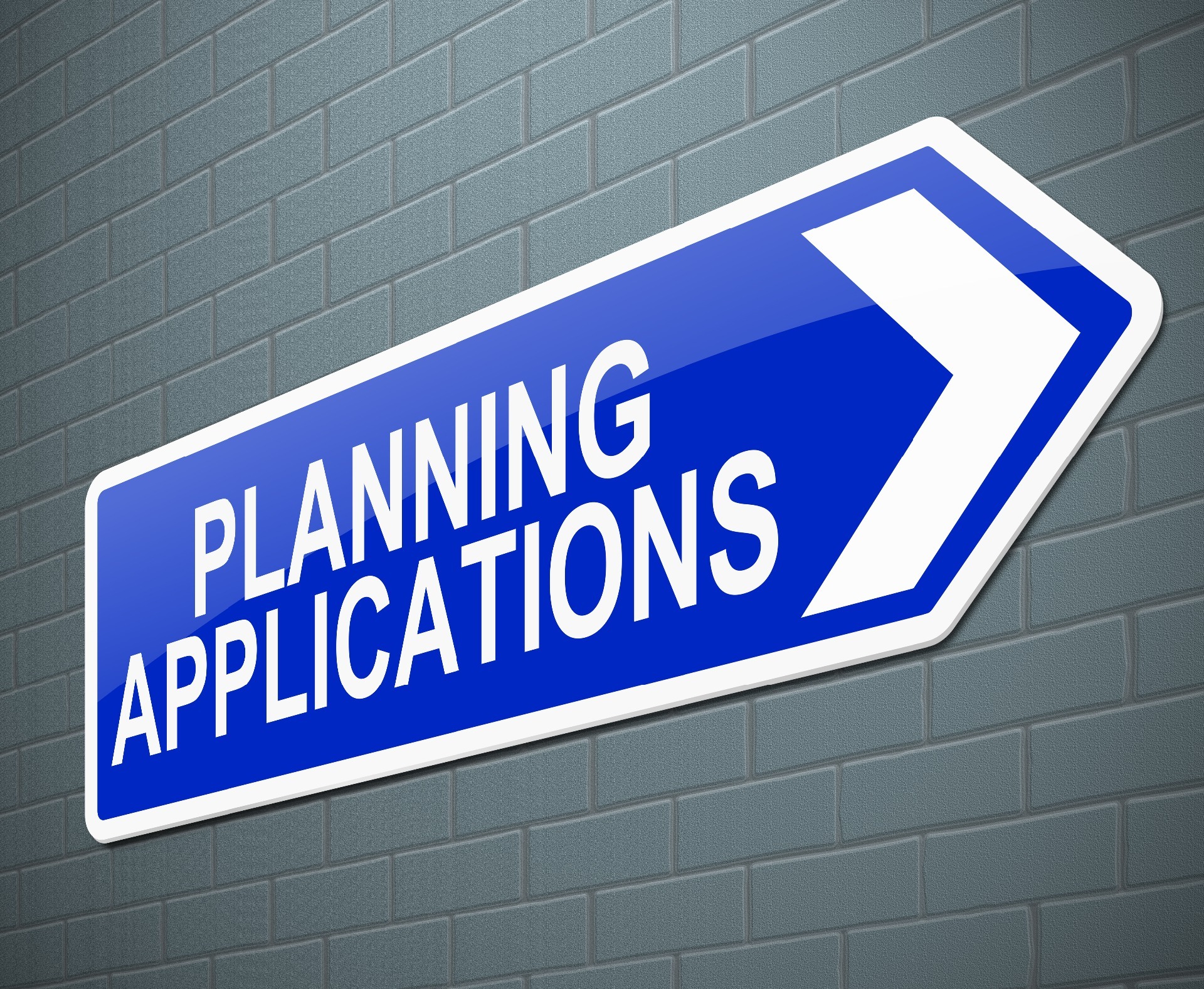 A blue and white sign in the shape of a directional arrow pointing towards 'Planning Applications'