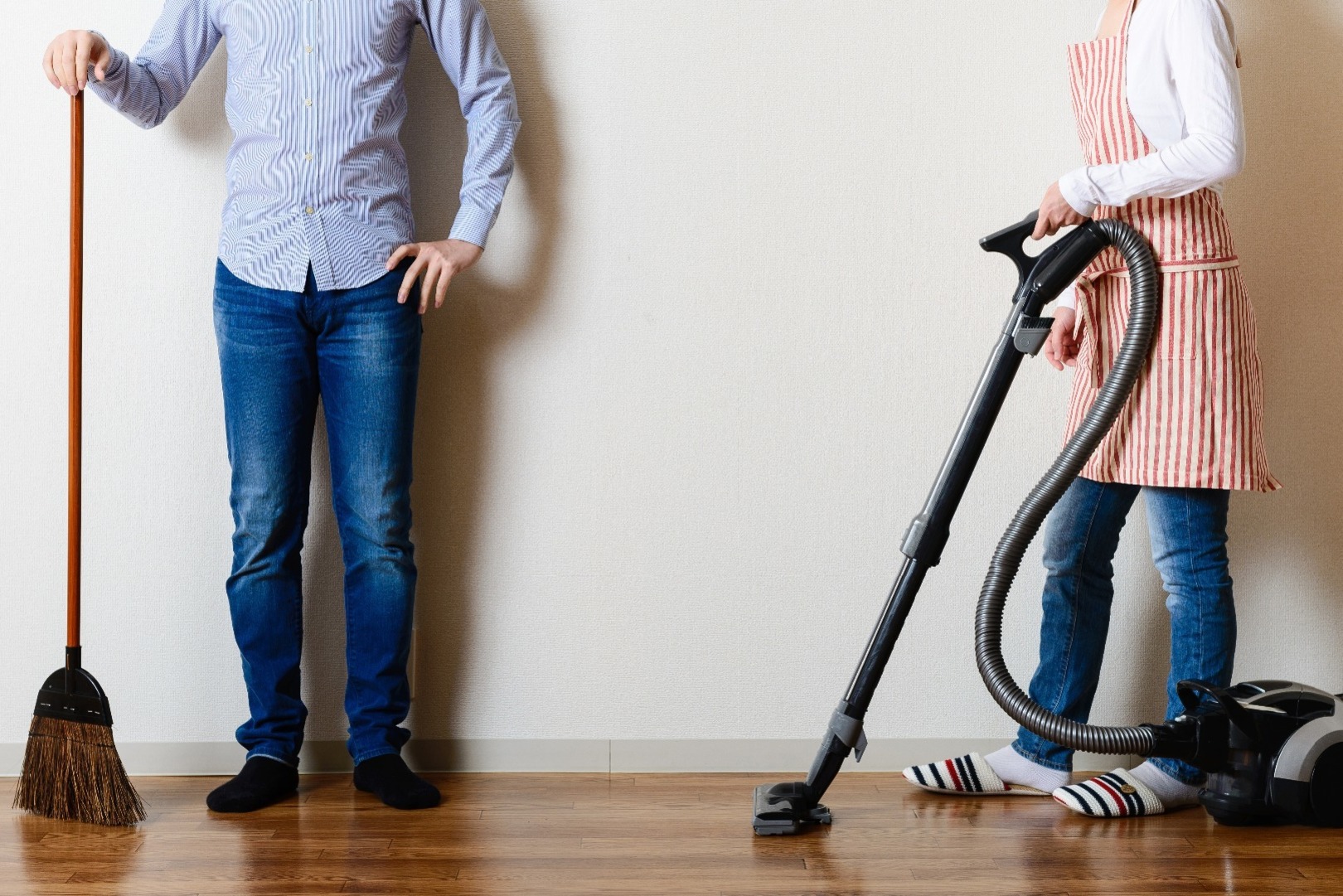 A couple with different household cleaning items, such as a broom and hoover.