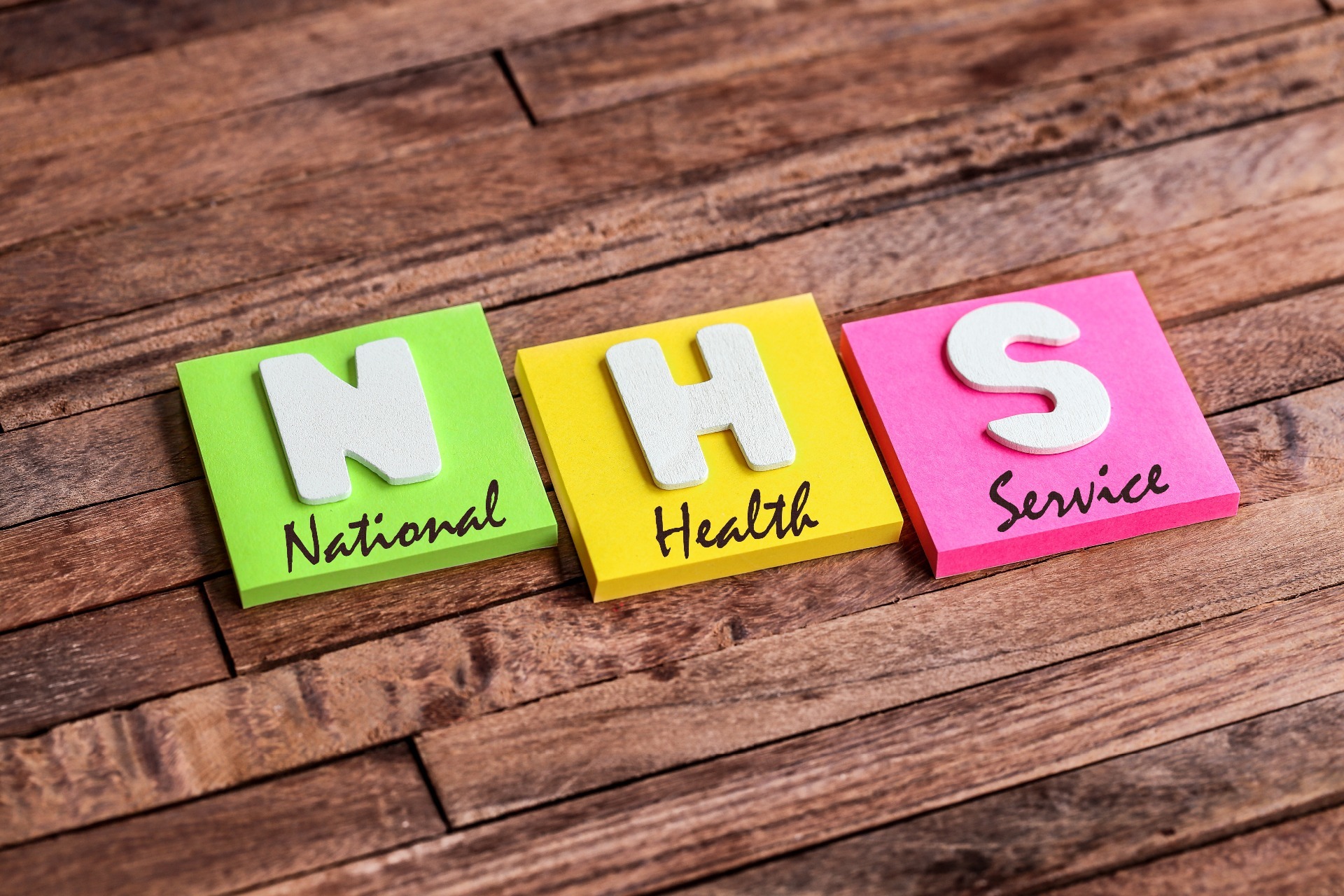 'National Health Service' on cut out squares, against a wooden background.