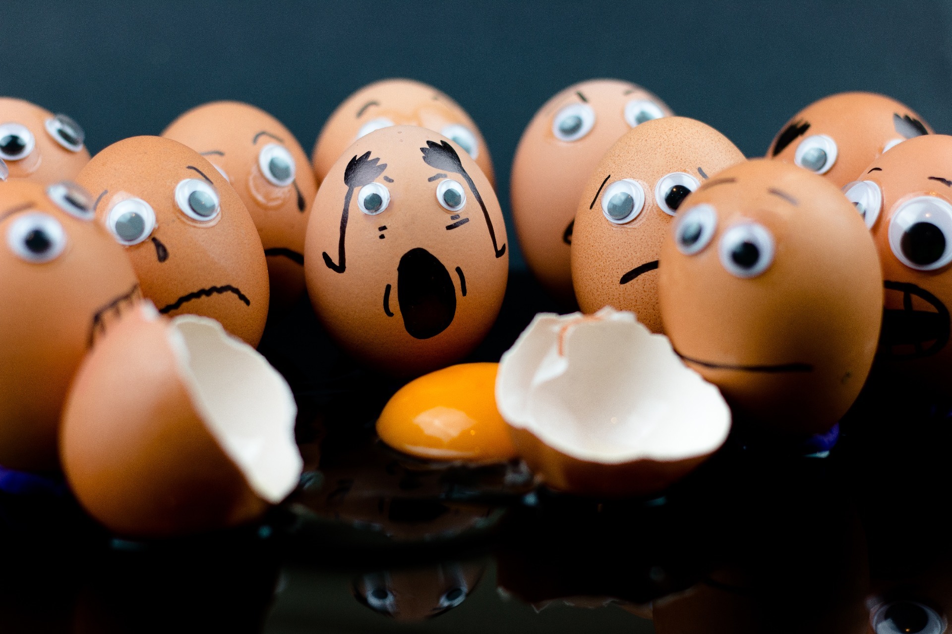 A dozen eggs, with sad and shocked faces drawn on, with a smashed egg in the middle; our No Win No Fee solicitors can assist with your injury at work compensation claim.