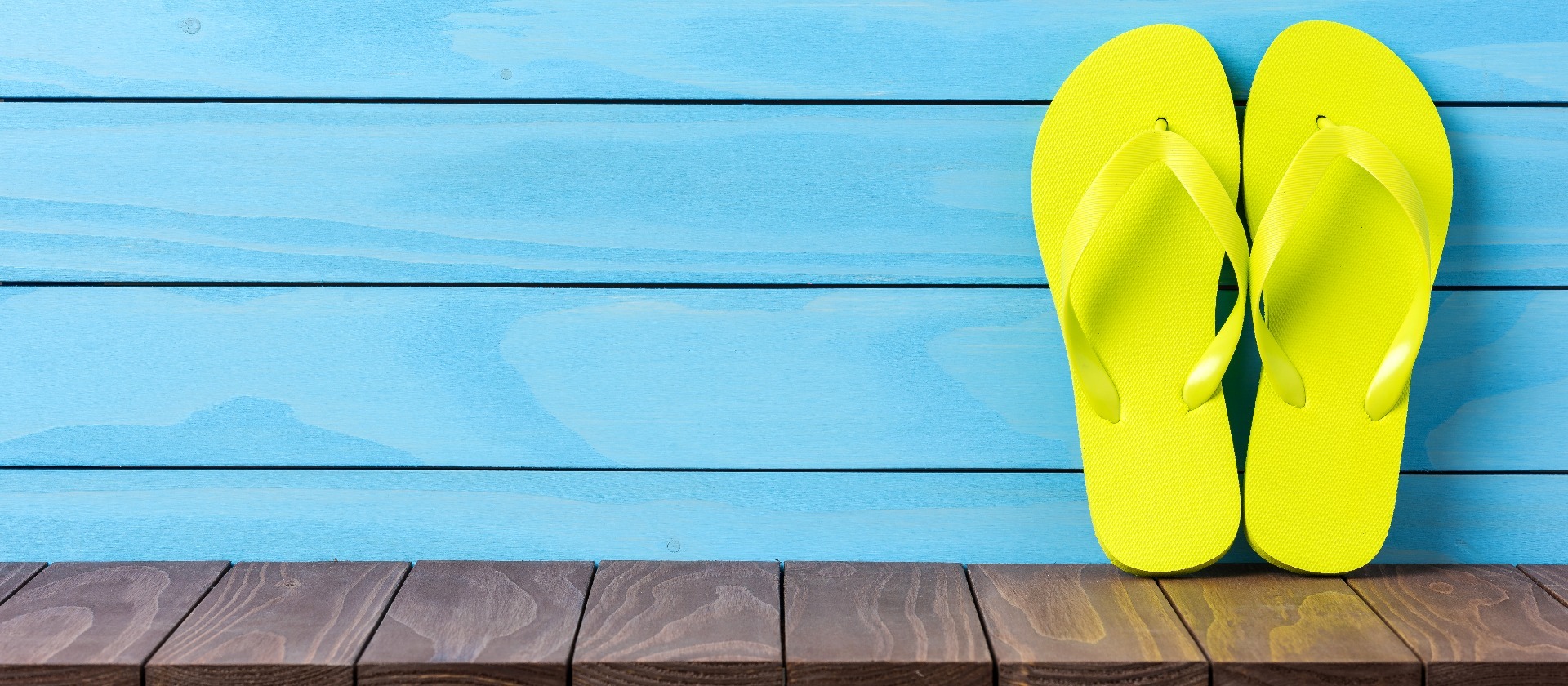 A yellow pair of flip flops, propped against a blue, wooden wall.