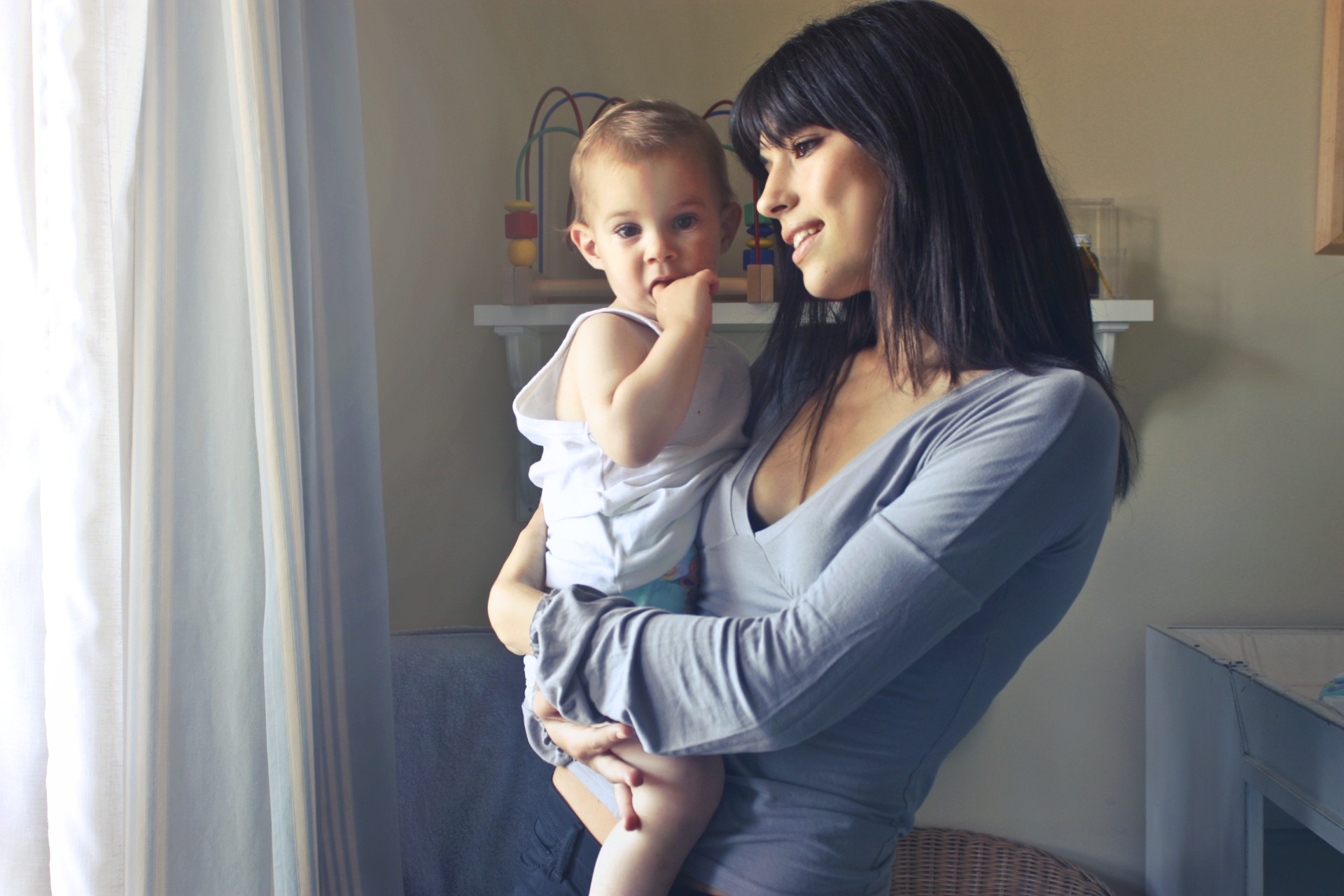 A woman holding a baby, looking out the window.