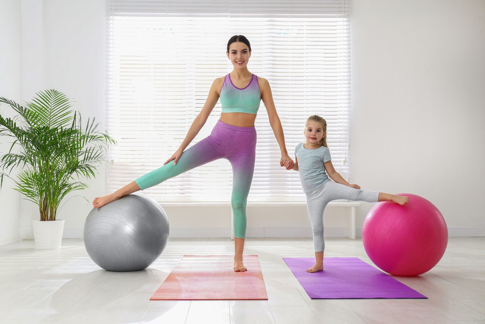A woman and a young girl exercising with yoga mats and large exercise balls inside a house.