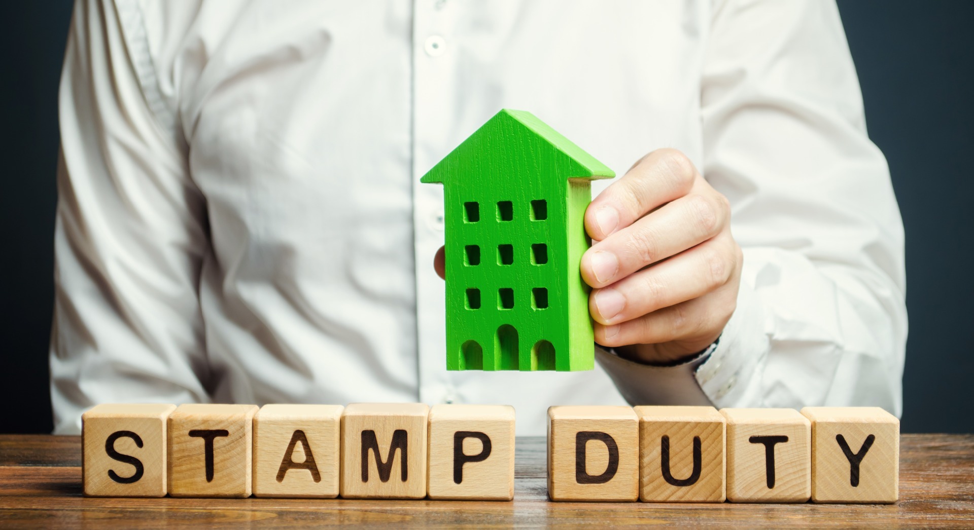 A green, wooden house, with word blocks spelling "Stamp Duty"; our Conveyancing Solicitors in Lancaster discuss the impact of downsizing your house on Stamp Duty.