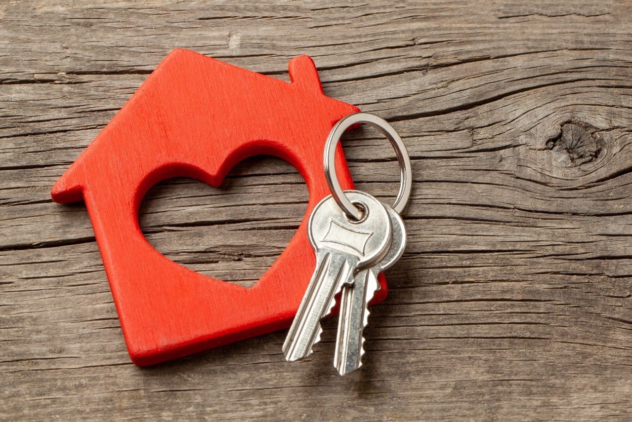 A wooden block of a house with a heart in the middle.  A set of keys rests on top.
