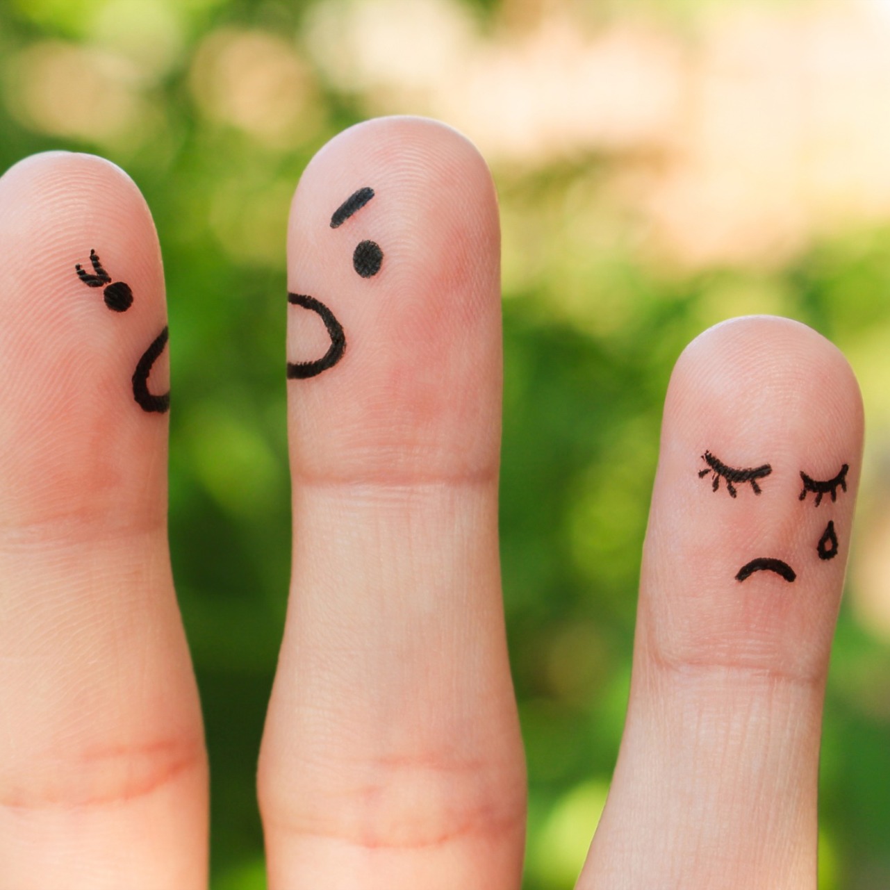 Two angry faces drawn onto fingers, next to a sad face drawn onto a finger
