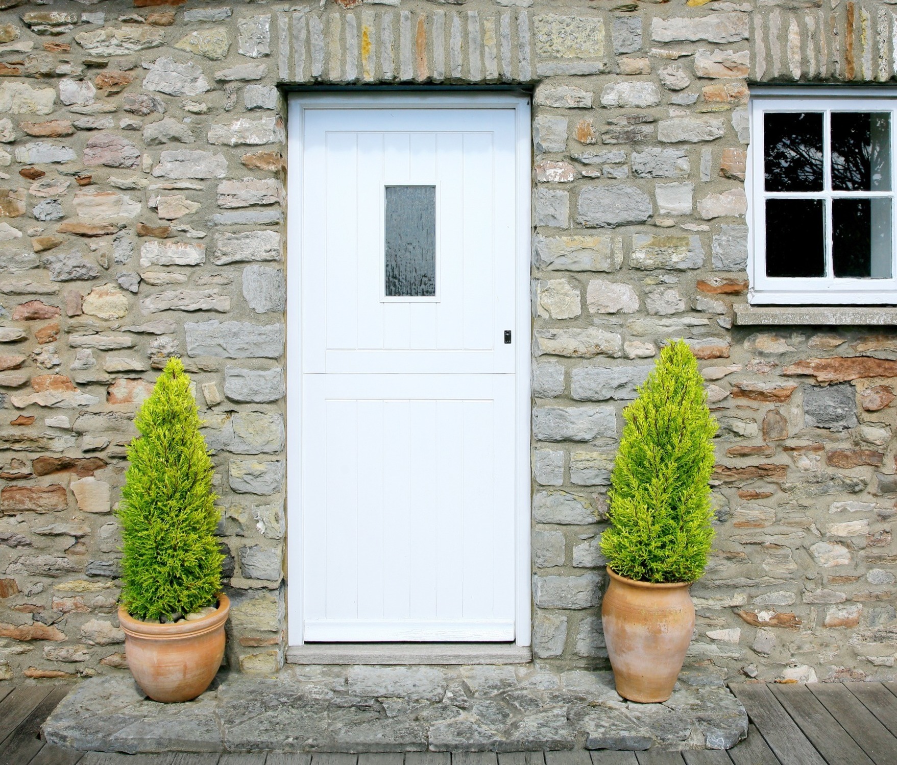 A stone-fronted house with a white door, with a plant either side.  Our Conveyancing Solicitors can assist with residential property purchases.  Follow this link to find out more.