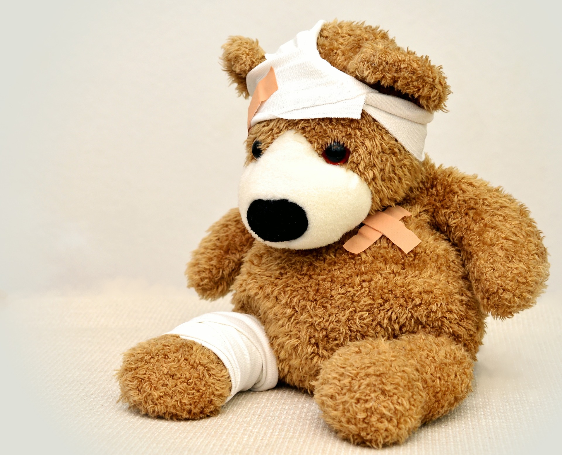 A teddy bear, with a bandage on his leg and head, and a plaster on his torso.
