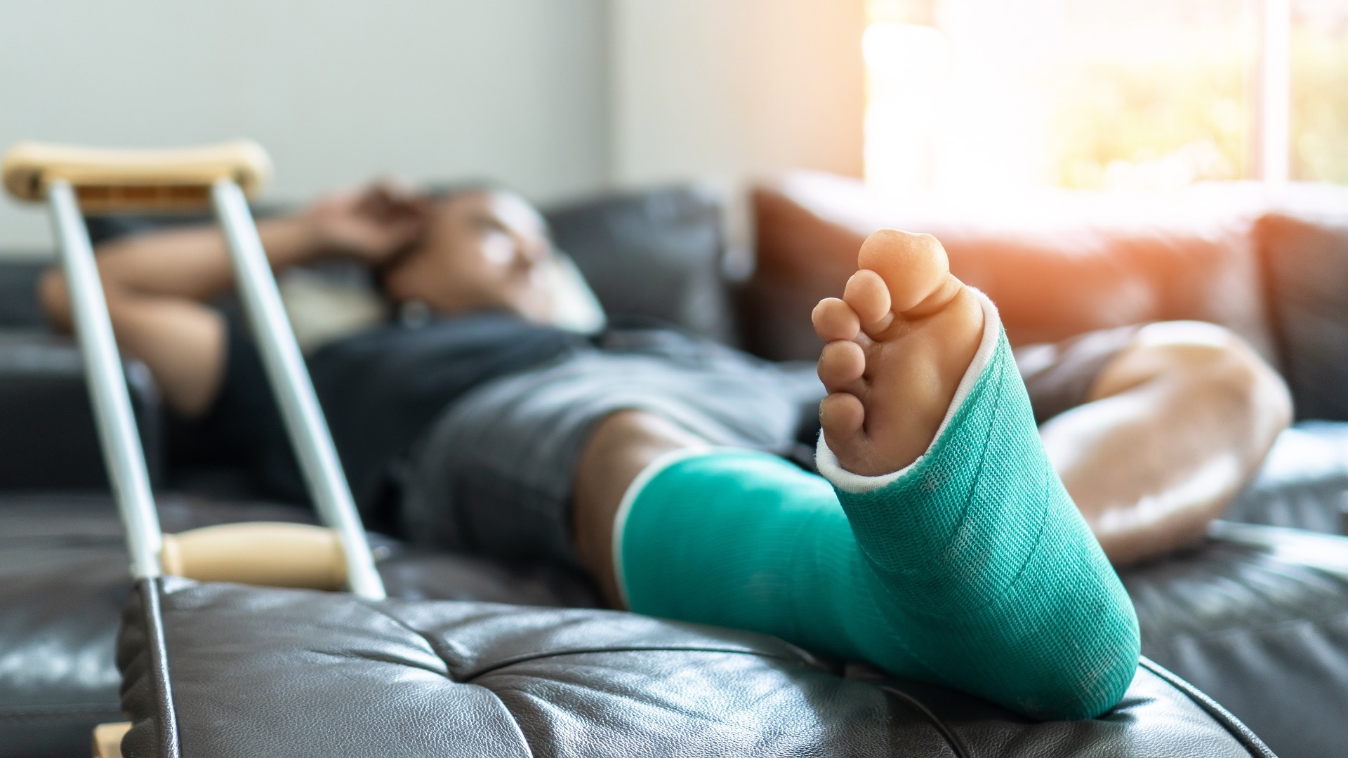A man with a broken leg, sat on a sofa.  Our Cycling Injury Claim specialists discuss common injuries caused to cyclists in Road Traffic Accidents.