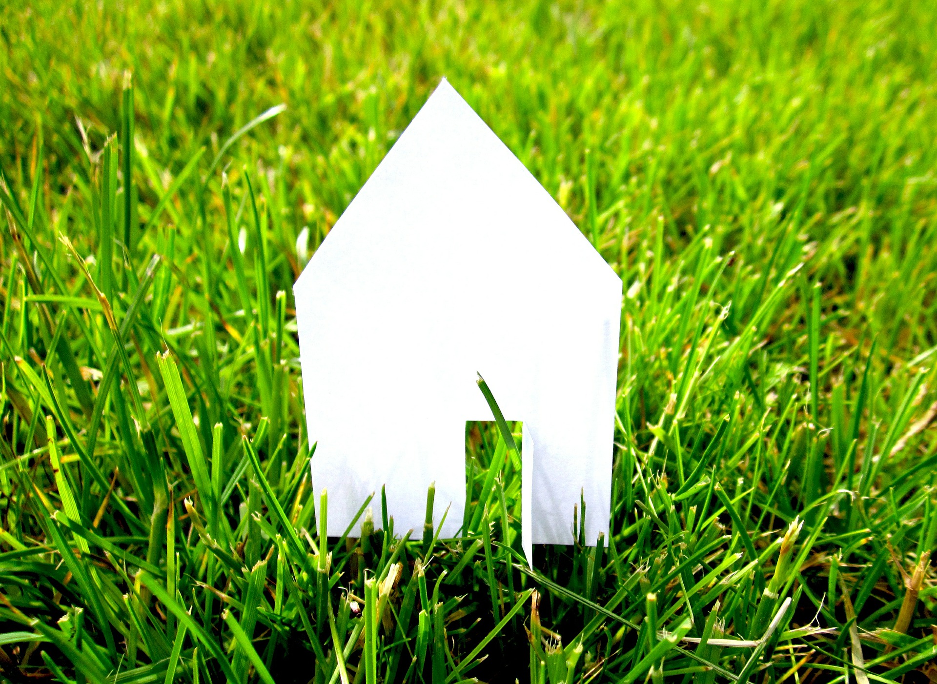 A white paper house in a green, grassy field; our Conveyancing solicitors discuss whether you should use the conveyancing solicitor recommended by your estate agent.